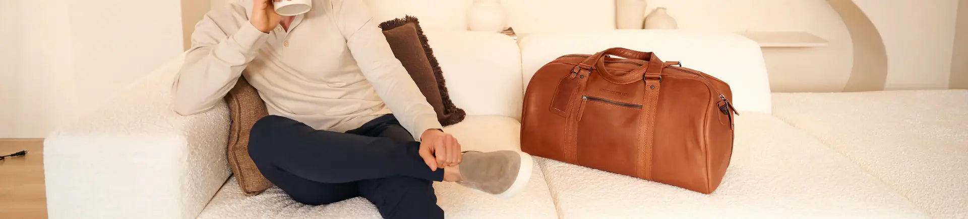 Brown leather travel bag styled on a light sofa in a refined living space